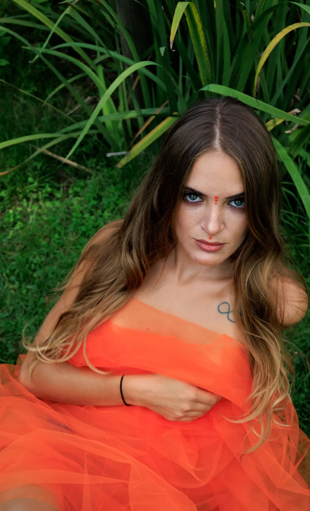 Una ragazza avvolta in un tulle arancione, sdraiata nell'erba.