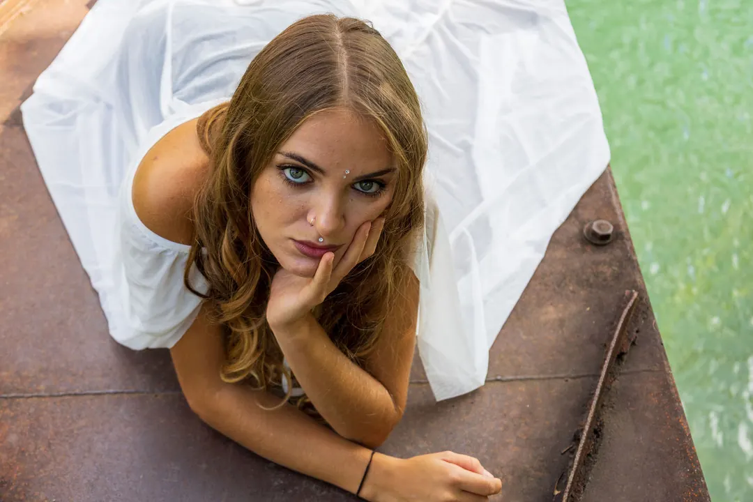 Una ragazza con un abito bianco sdraiata su un pontile, con il mento appoggiato alla mano.