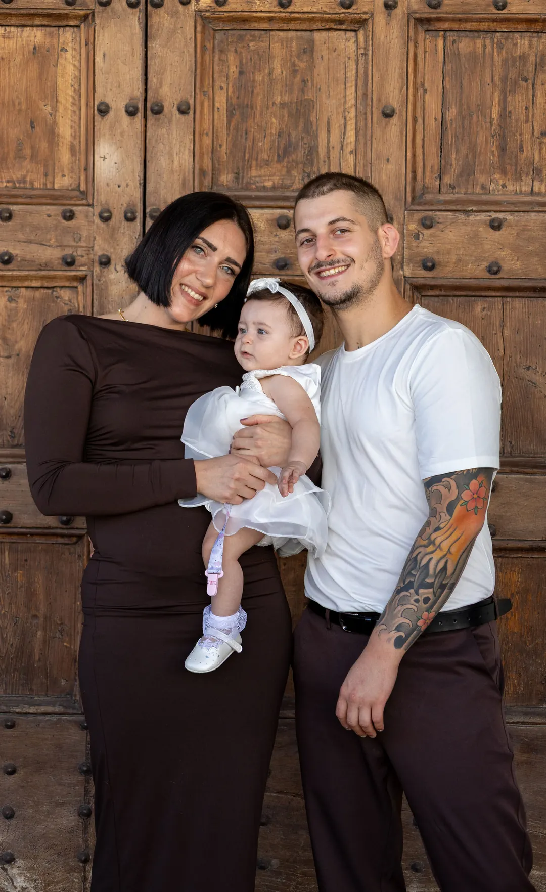 Una famiglia con la bimba in braccio davanti a un portone di legno.