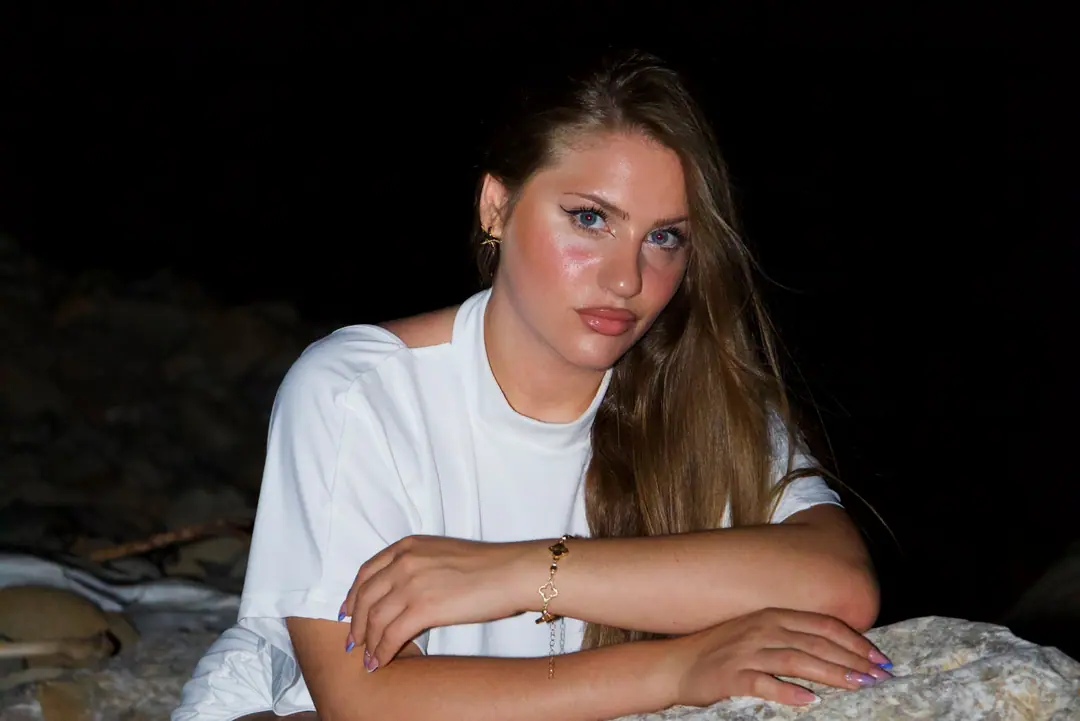 Di notte, con il flash: una ragazza in bianco appoggiata a uno scoglio guarda dritto in camera.